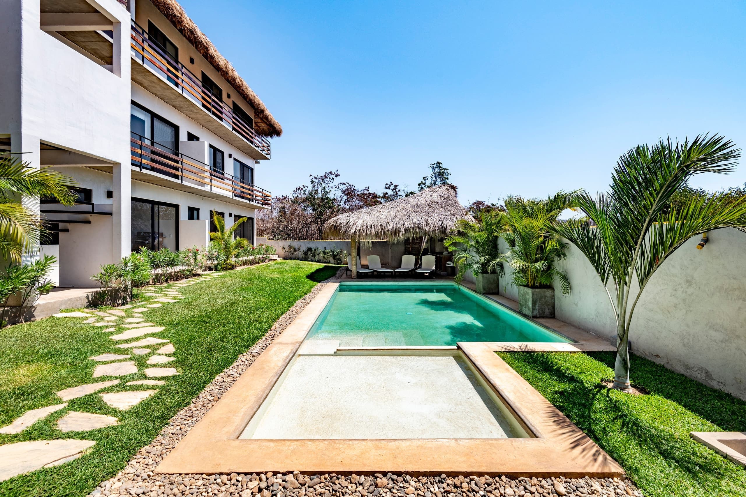 Alberca del condominio rodeada de jardín y palmeras
