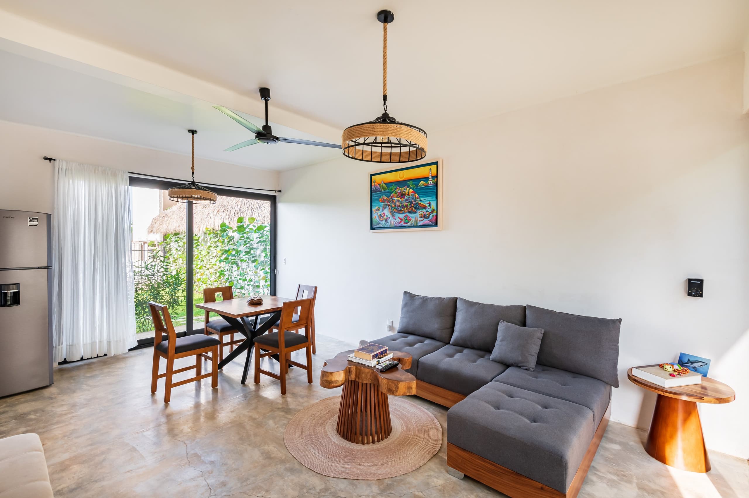 Estancia con sala gris, comedor de madera y ventanal al jardín
