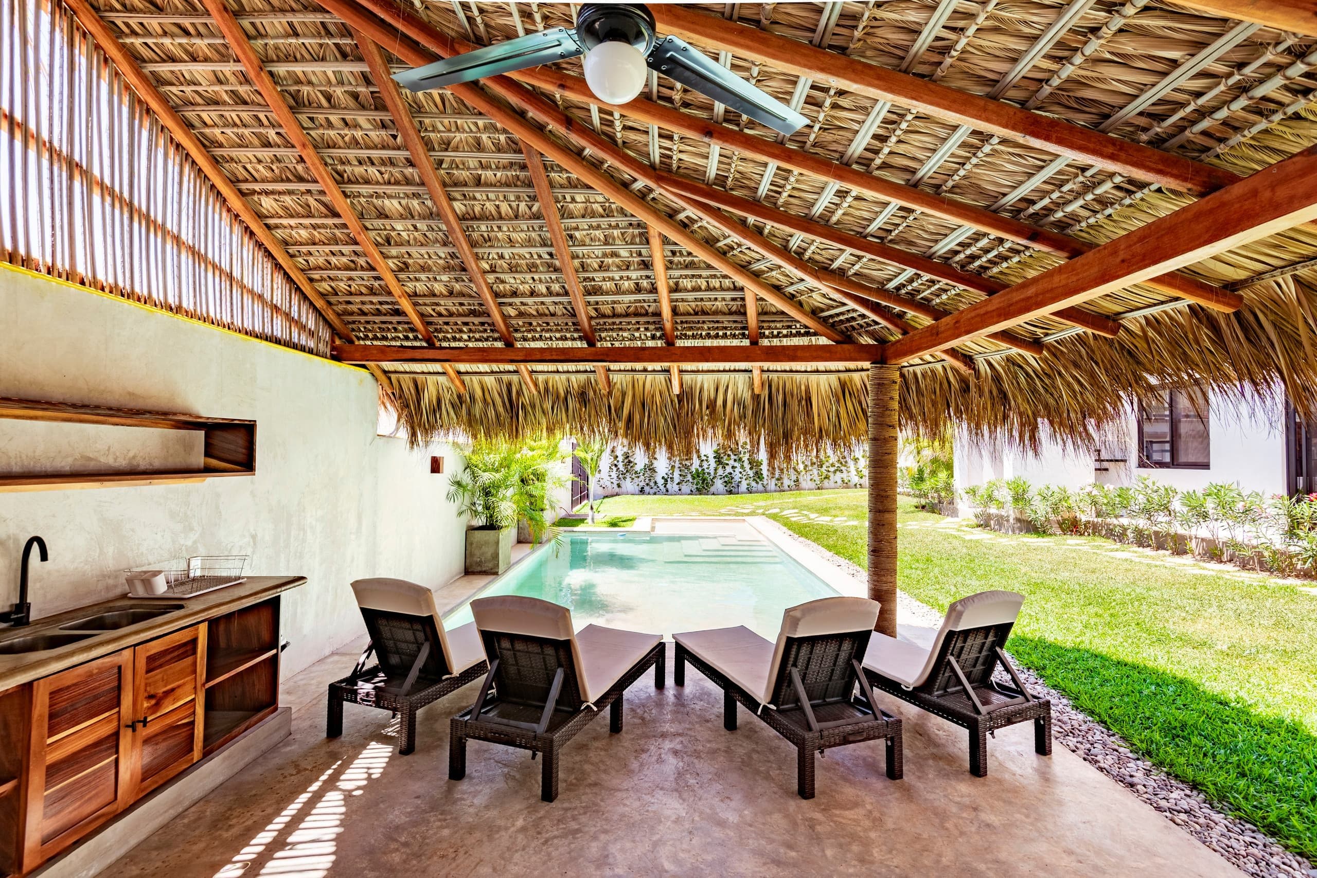 Palapa con cocina exterior y camastros junto a la alberca del condominio